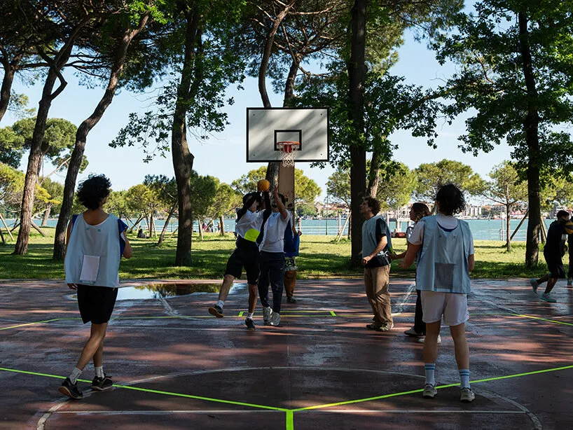 Un grupo de personas con petos claros juega uno de los deportes diseñados por Gabriel Fontana sobre una cancha exterior con líneas verde flúor pintadas encima del marcado original.
