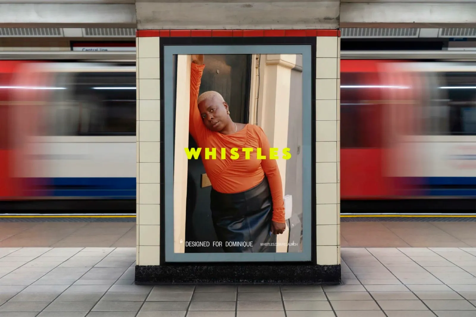 Póster de la campaña de Whistles en una estación del metro de Londres: Dominique, una de las 50 clientas, apoyada en el marco de una puerta con un top naranja, el wordmark en amarillo Lemonade y la línea "Designed for Dominique".